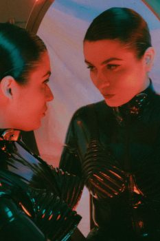 Mistrix Violeta Félix looking in a mirror while wearing a black latex catsuit.